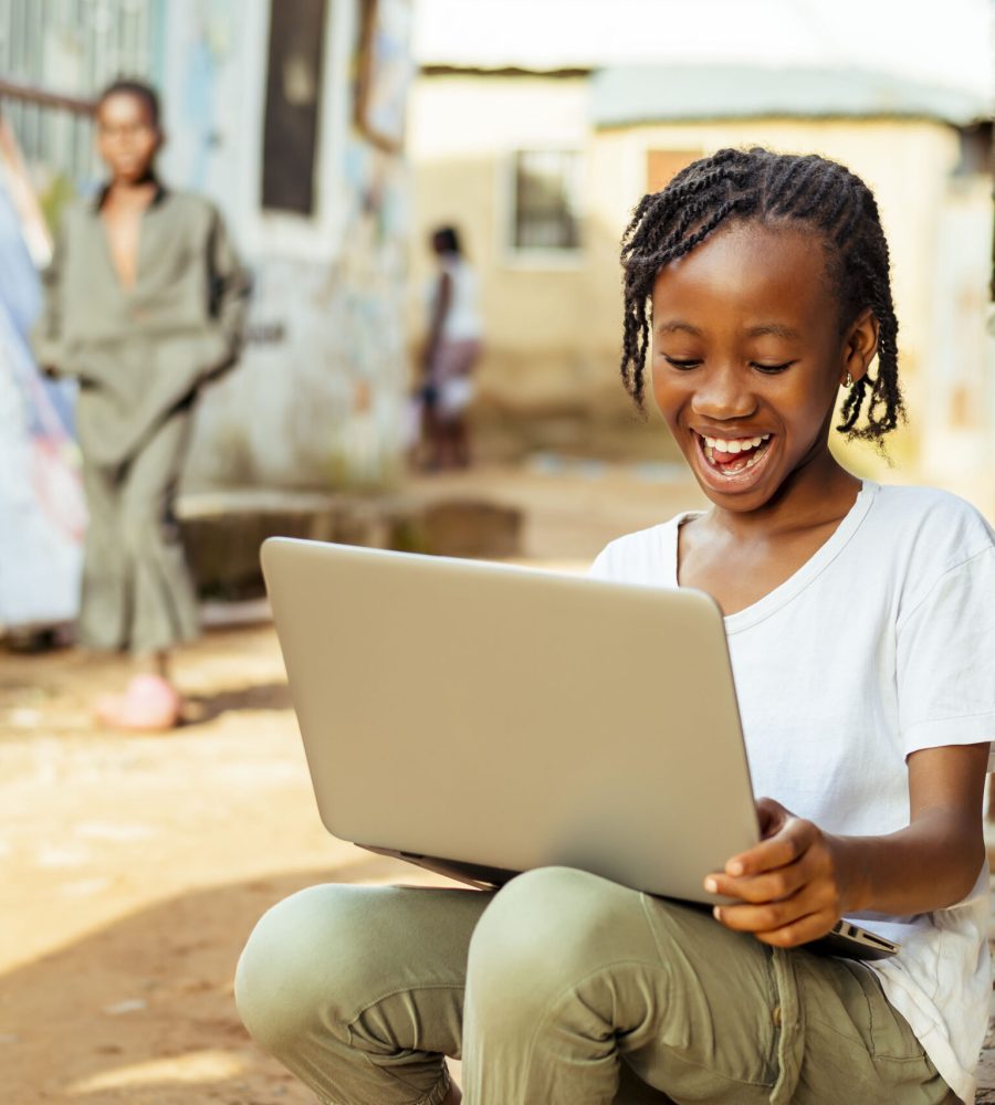 excited young African child sitting on the ground with a laptop and a cell phone
